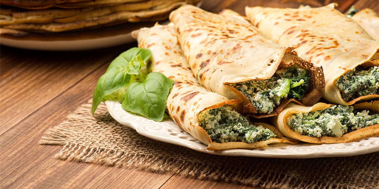 Pancakes filled with spinach and cheese on the wooden surface.